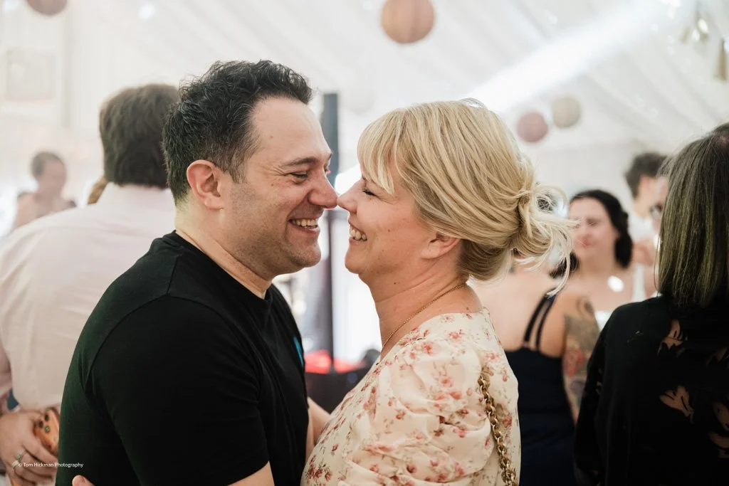 A man and woman smiling and touching foreheads at a social gathering.