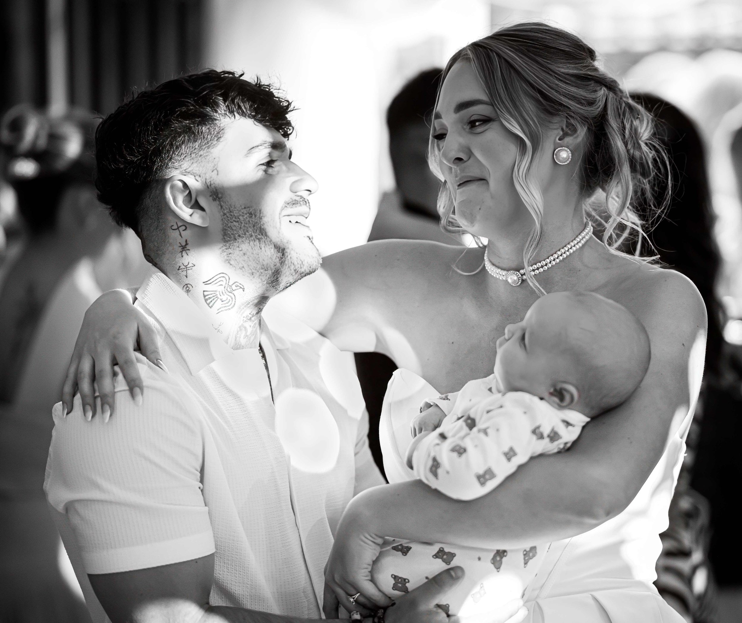 A black and white photo of a man and woman smiling at each other, dancing closely with arms around each other, in a social setting.
