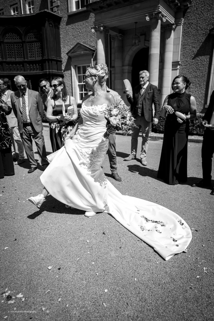 A bride in a wedding dress stepping on glass outside a building surrounded by wedding guests.