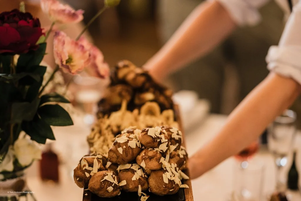 Display of assorted chocolates with white chocolate shavings on top at a dessert table, floral arrangement visible on the left.