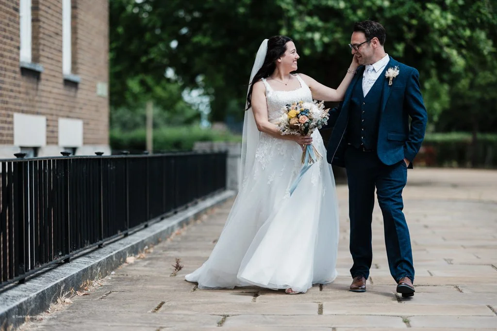 Bride and groom walking on a sidewalk during their wedding day, laughing and looking at each other.