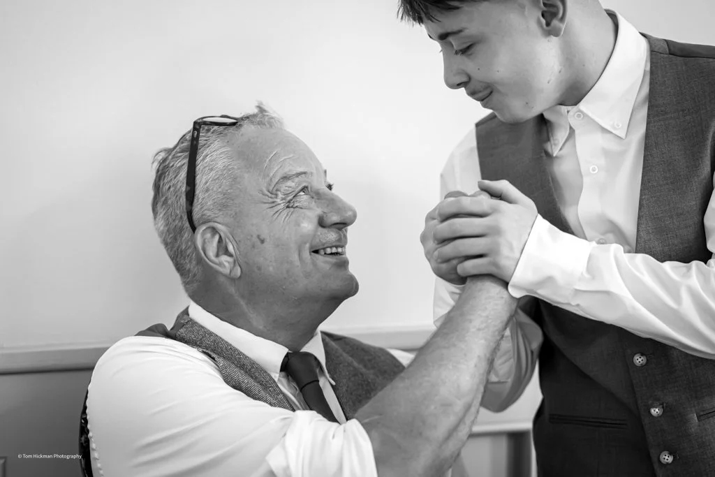 An elderly man smiling while shaking hands with a younger man in a professional setting.