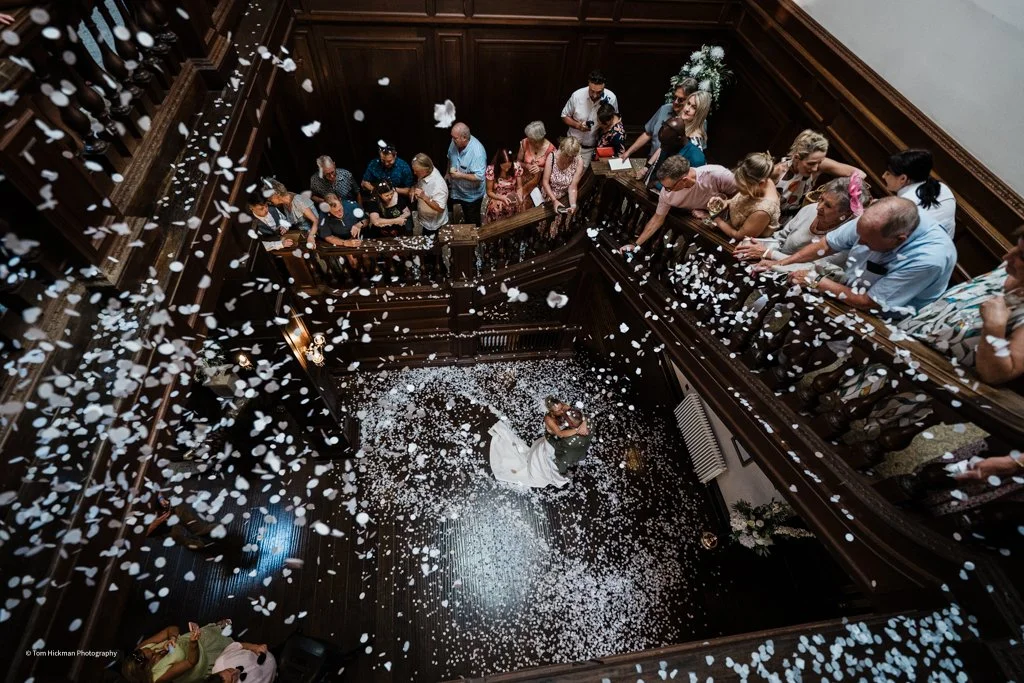 A couple dancing on the floor of a crowded, multi-level wooden staircase at a wedding reception, surrounded by confetti.