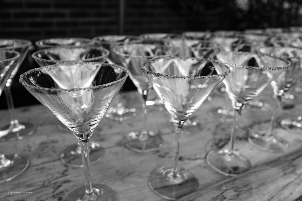 Multiple empty martini glasses with salted rims arranged on a wooden surface.