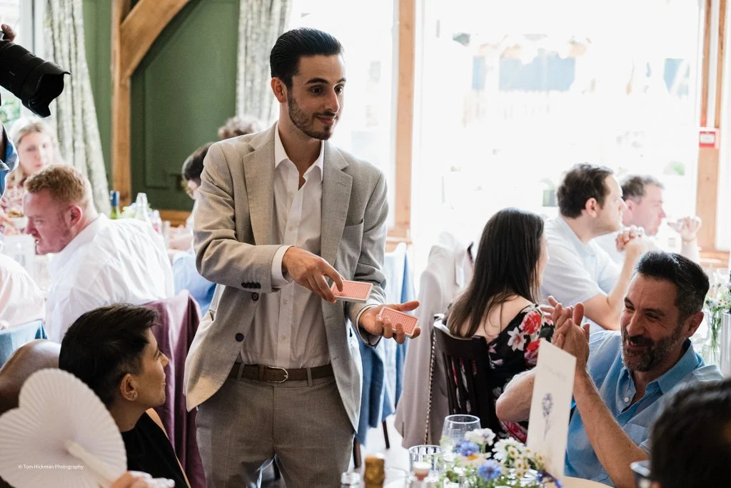 A magician performing a card trick at a wedding reception while guests watch and applaud.