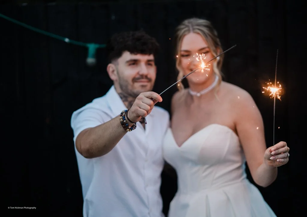 A couple at a celebration, holding sparklers with a dark background.