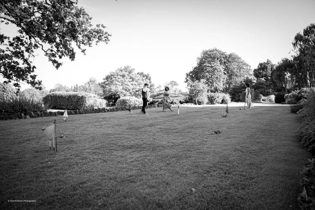 People playing mini-golf outdoors in a park with trees and bushes.