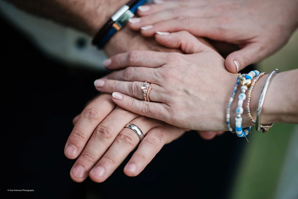 Close-up of three hands stacked on each other, showing wedding rings and colorful bracelets, symbolizing unity and celebration.