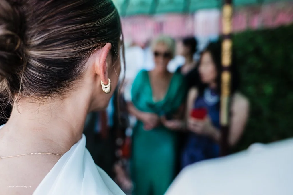 Close-up of a woman's head and shoulder with earrings, facing a group of women in the background at a social gathering.