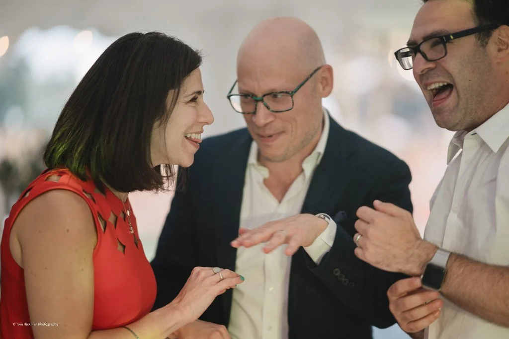 Three people engaged in a lively conversation, smiling, indoors with blurred background.