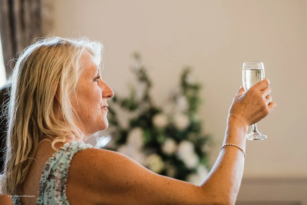 An elderly woman with blonde hair raising a glass of champagne or sparkling wine in a toast.
