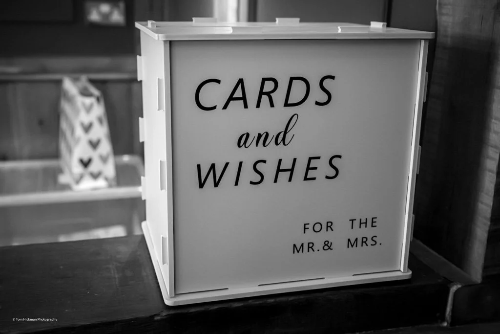 A white, rectangular box with the text 'CARDS and WISHES for the MR. & MRS.' on the front, placed on a wooden surface in a rustic setting.
