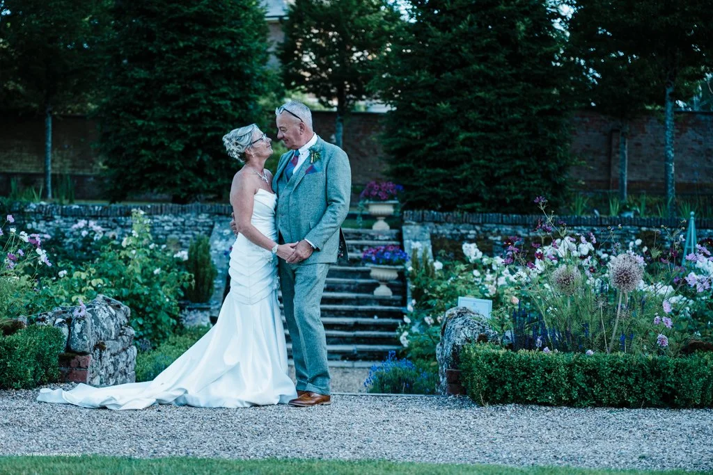 An elderly couple dressed in wedding attire holding hands in a garden