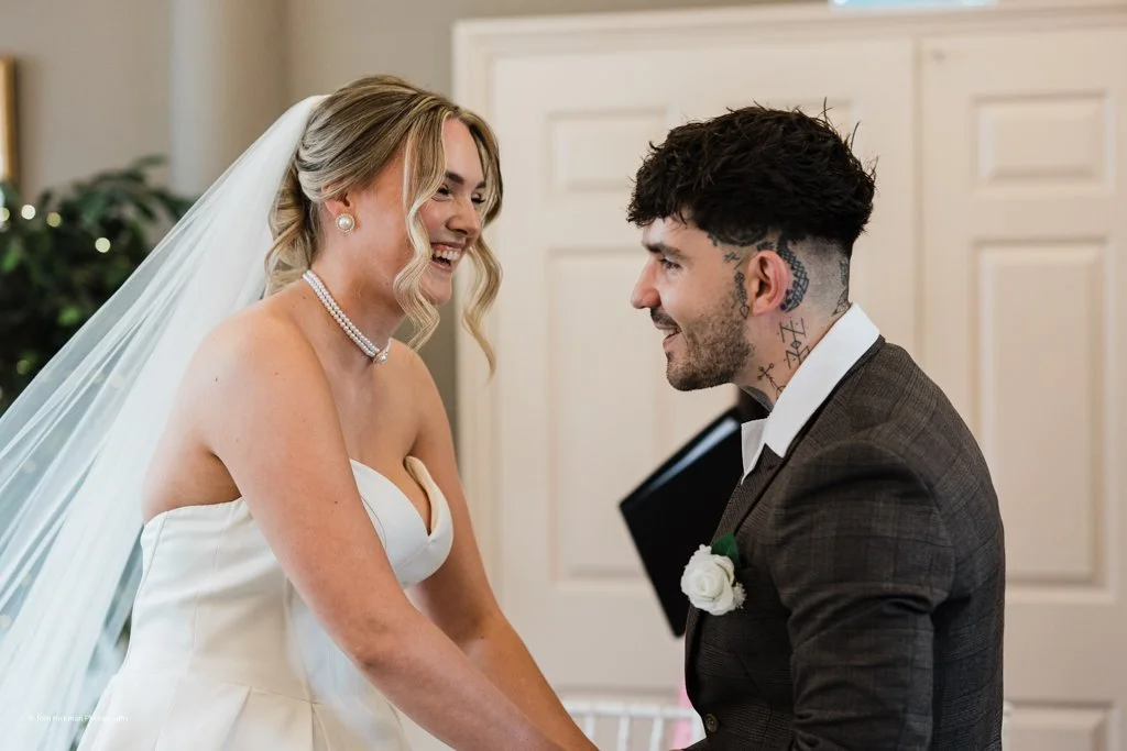 Bride and groom smiling at each other during wedding ceremony.