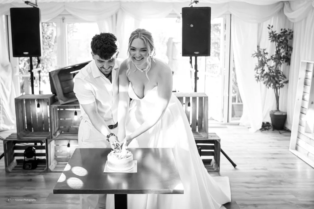 A bride and groom cutting a wedding cake together in a decorated venue.