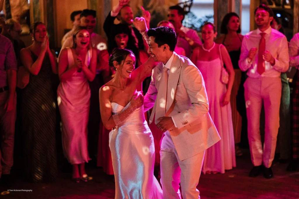 Couple dancing at a wedding reception with surrounded guests clapping and smiling.