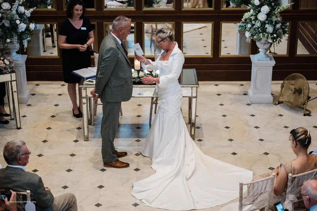 A bride and groom exchanging vows during a wedding ceremony in a decorated indoor venue with floral arrangements.