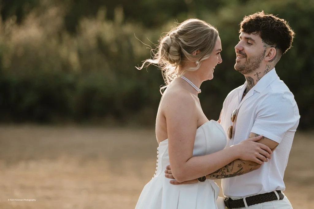 A bride and groom looking at each other and holding hands outdoors during daytime.