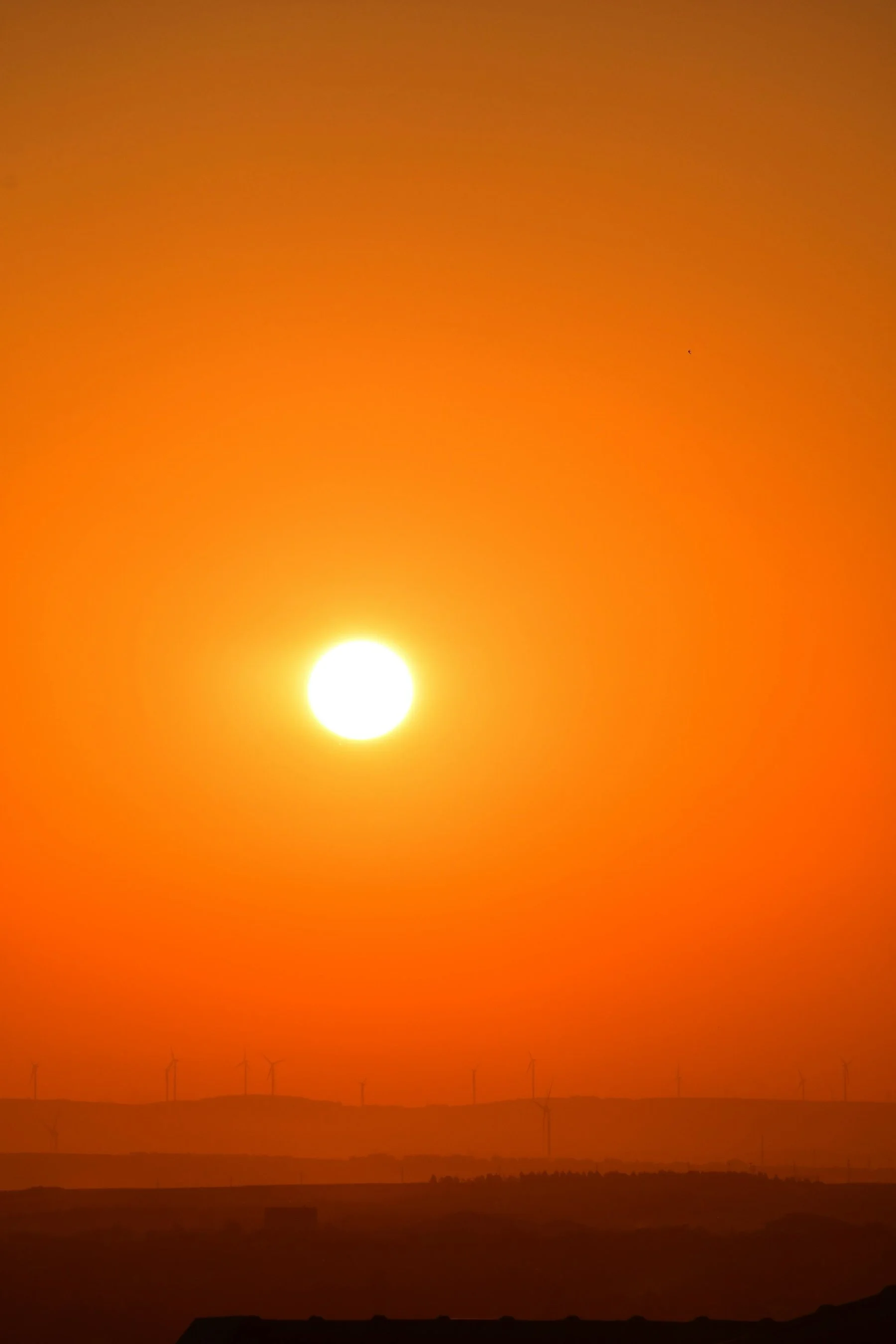 Sunset over rolling hills with wind turbines in the distance, orange sky.