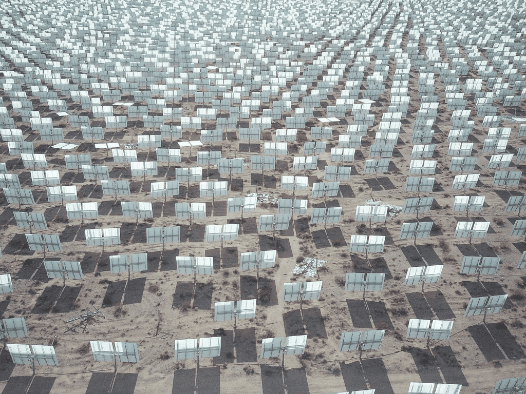 An expansive solar farm with numerous solar panels arranged in neat rows on a desert landscape.