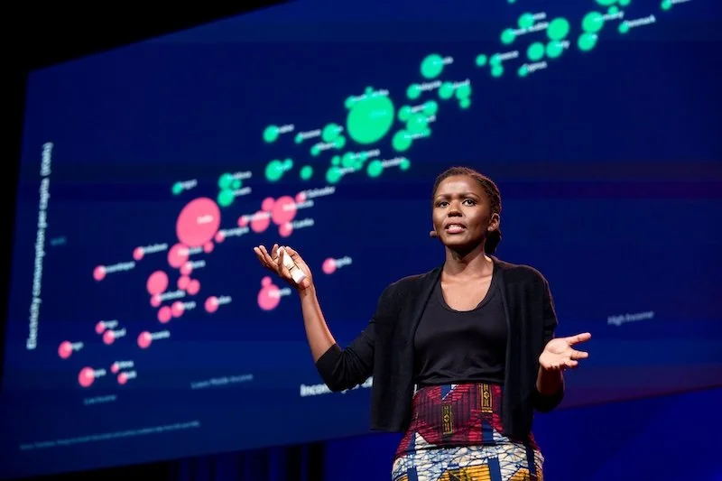 A woman giving a presentation on a graph with green and pink circles on a large screen.