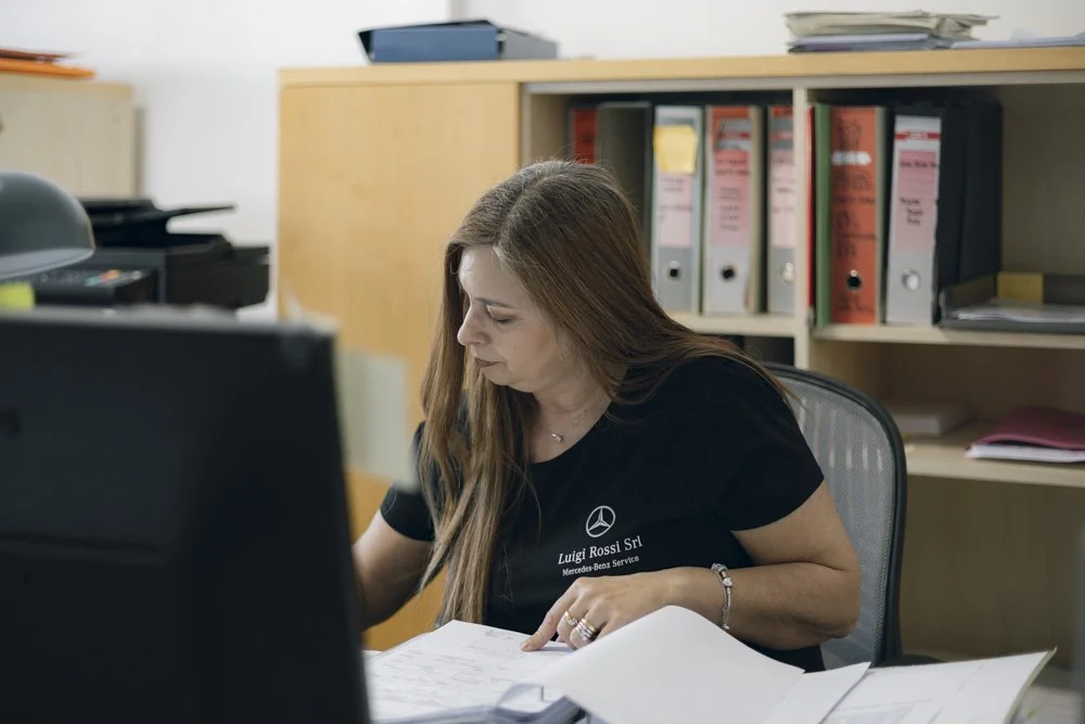 Donna seduta alla scrivania al lavoro, con cartelle e documenti, in un ufficio.