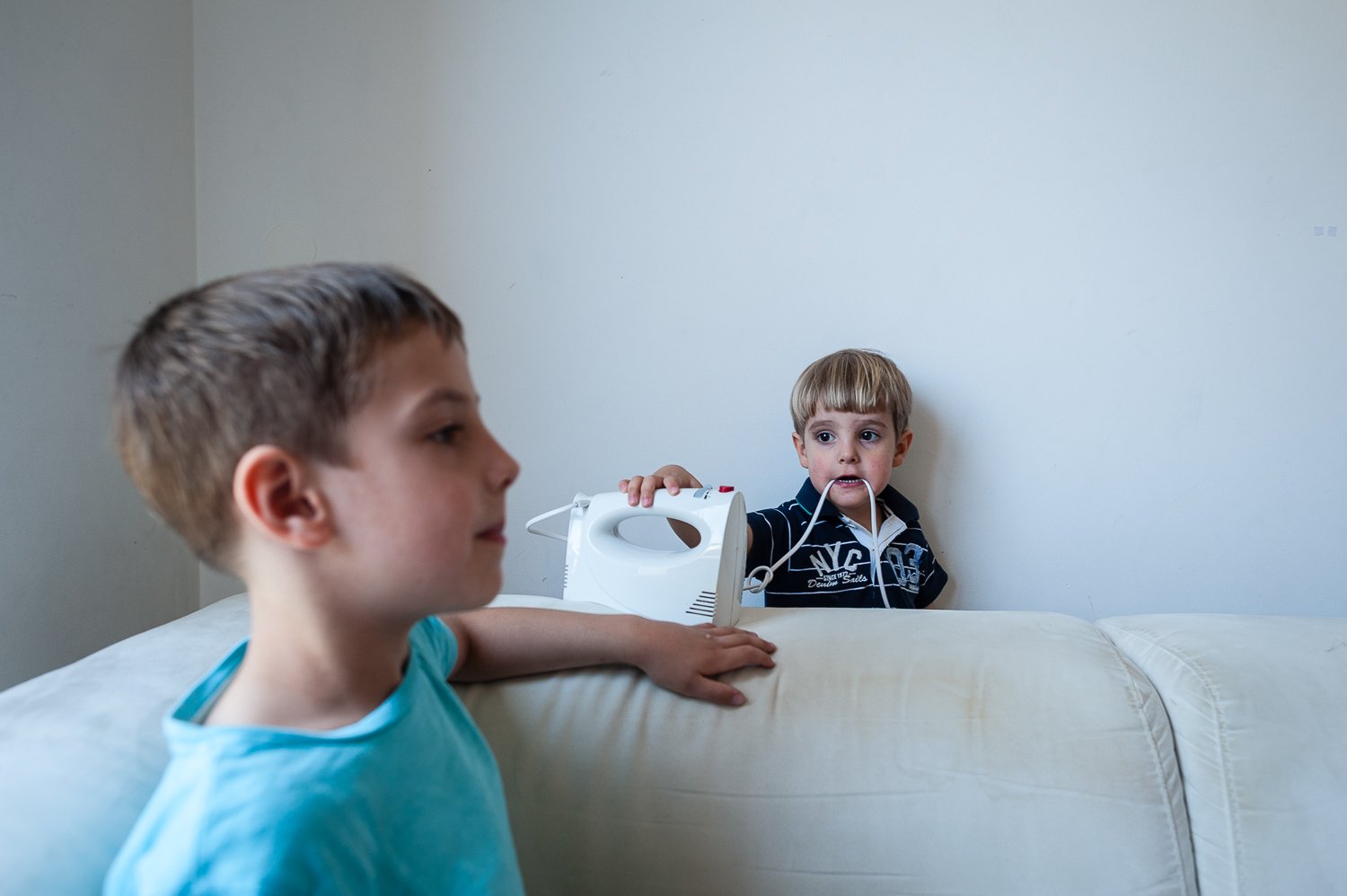 Dva mlada fanta, eden v svetlo modri majici in drugi v temni jakni z zadrgo, sta v sobi. Fant v jakni drži mešalnik. dokumentarno fotografiranje