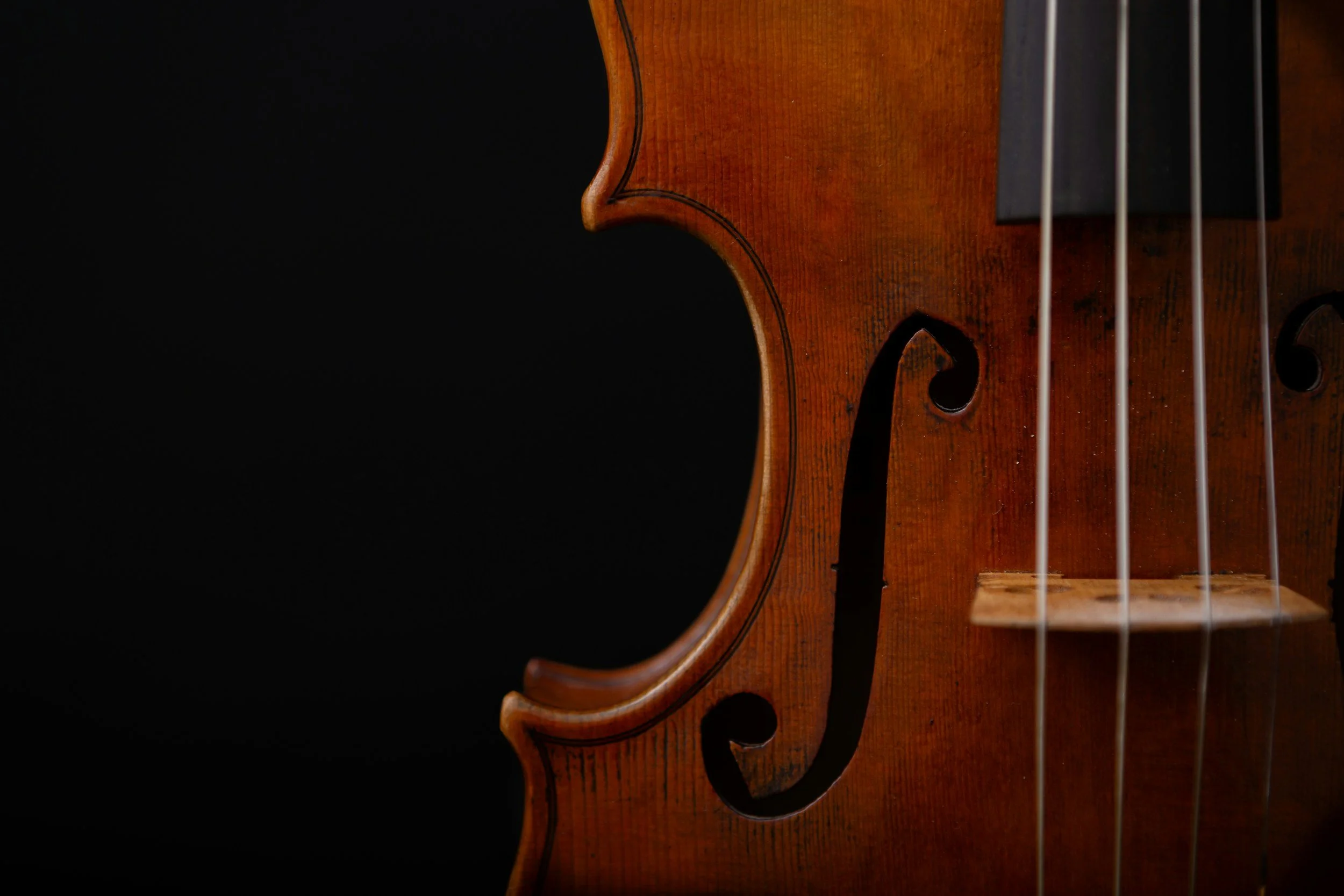 Close-up of a wooden violin body with four strings and a decorative sound hole, set against a black background.