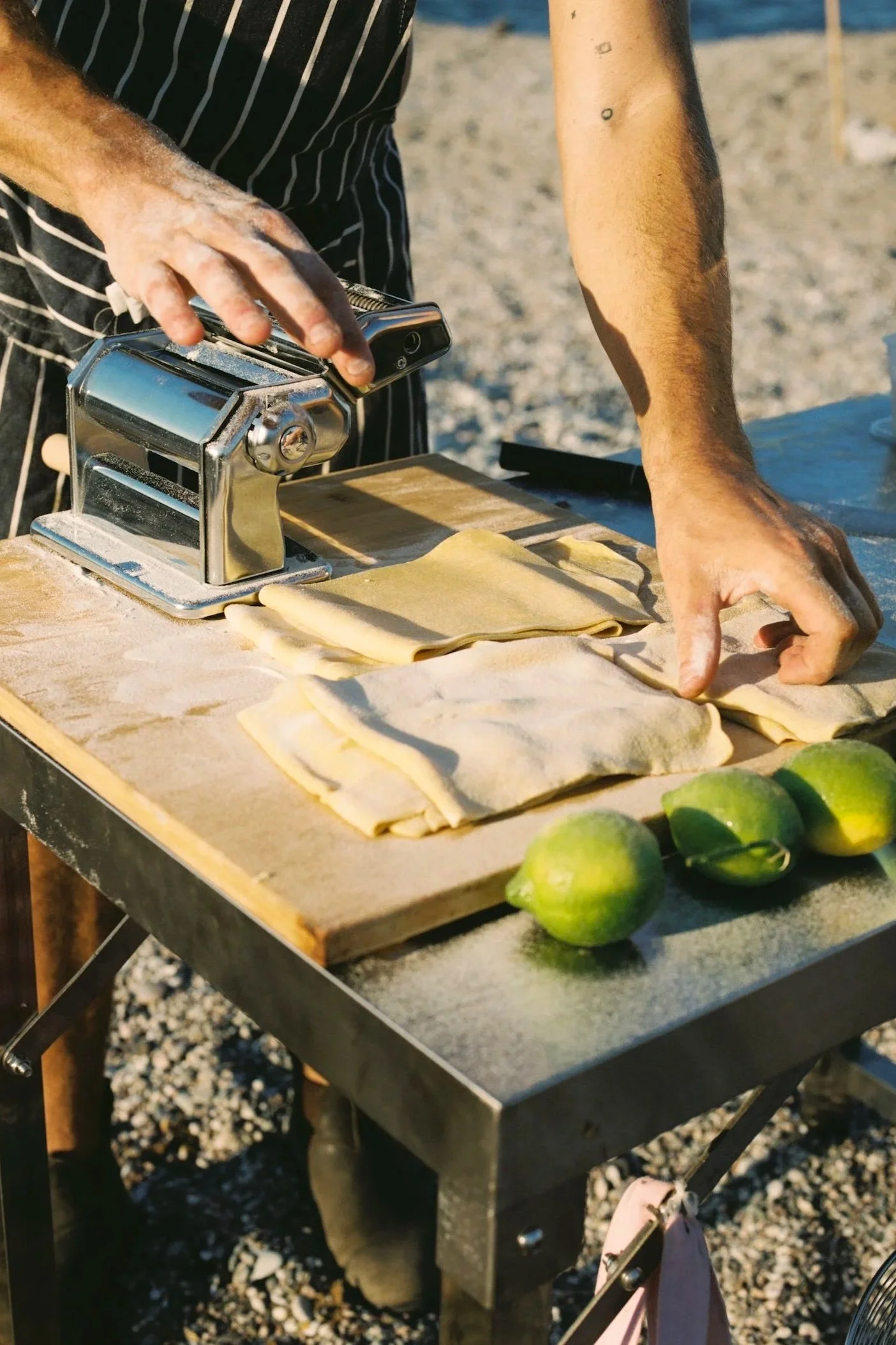 Person making ravioli pasta on outdoor table with green lemons nearby.