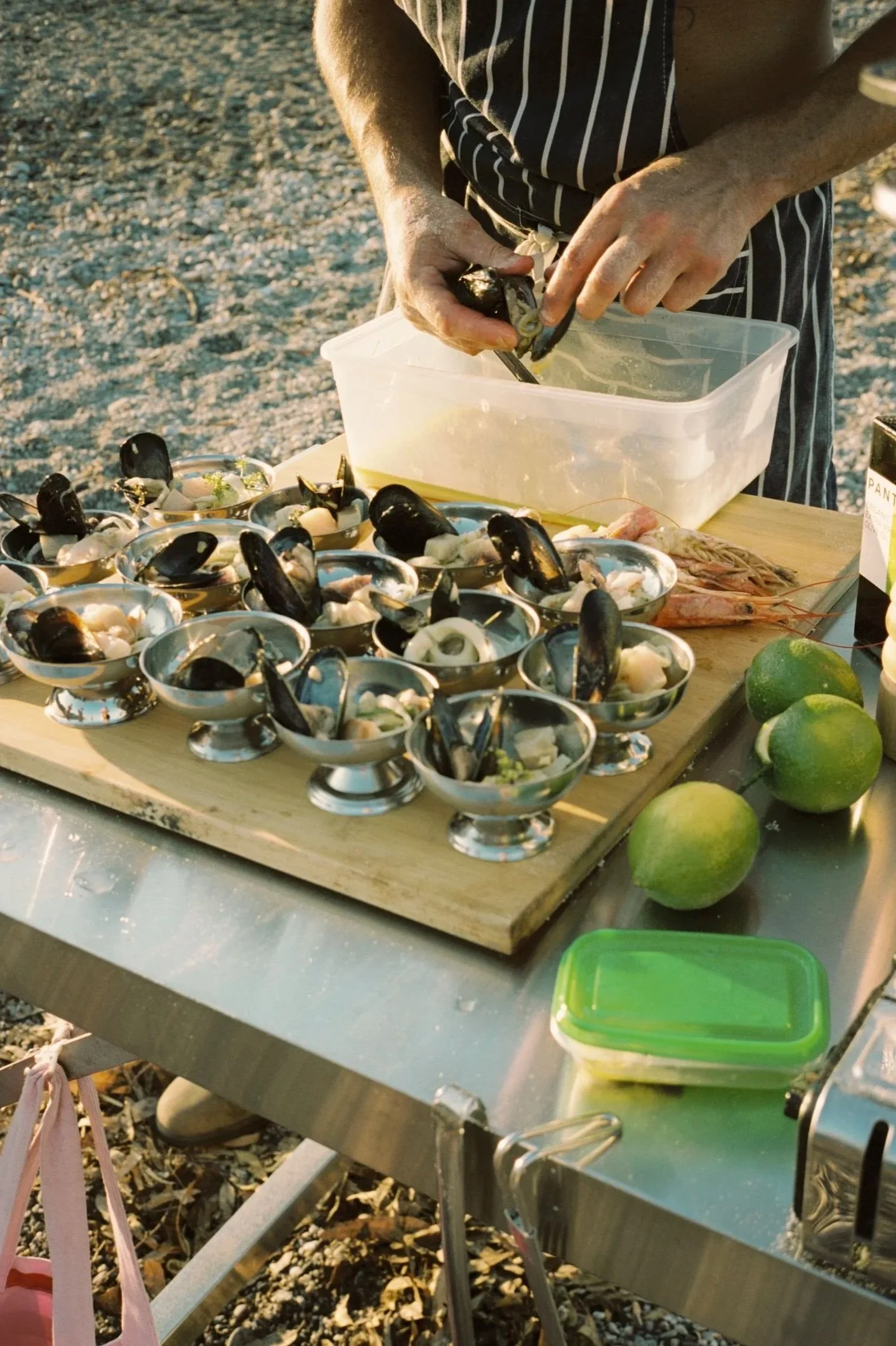 Person preparing seafood, likely mussels, on a table outdoors, with lime fruit nearby