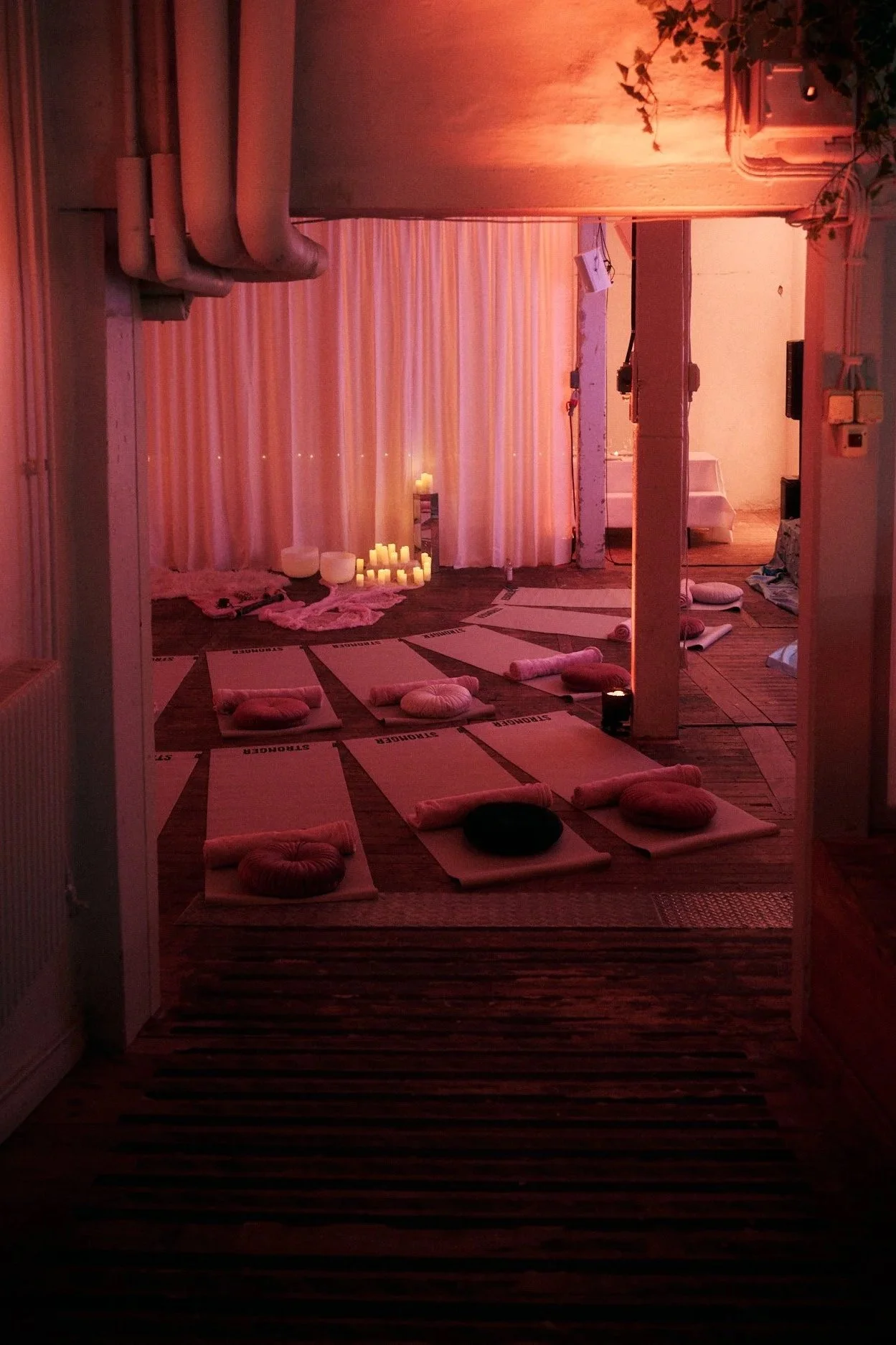 A cozy yoga or meditation studio with mats, cushions, and candles, set up for a relaxing session with soft pink lighting and candles in the background.