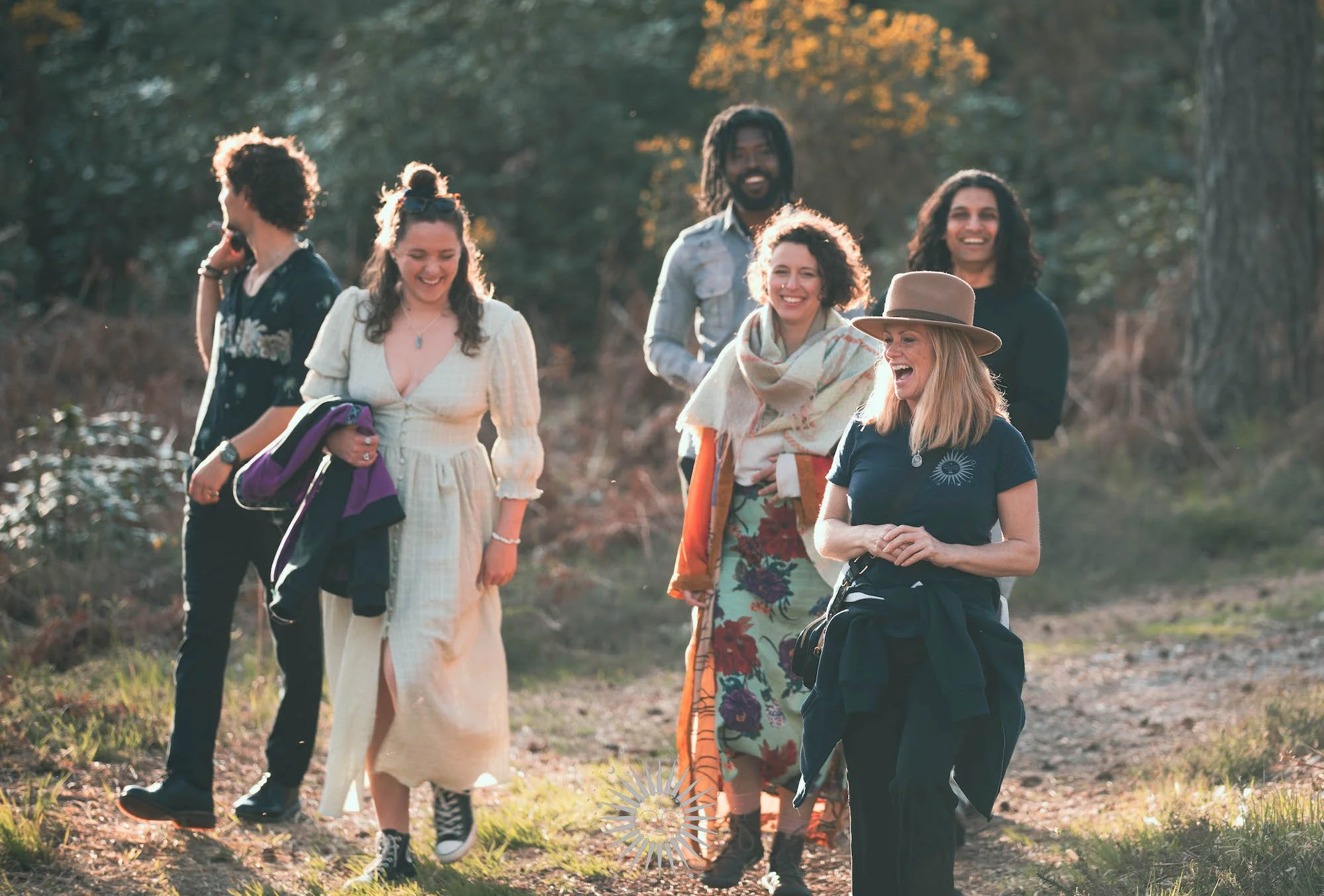 A group of six friends walking and laughing outdoors in a forested area during daytime.