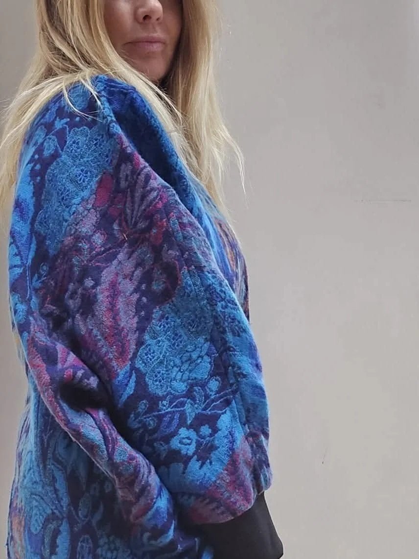 Close-up of a woman wearing a colorful, patterned jacket with blue, purple, and red hues, standing against a plain background.