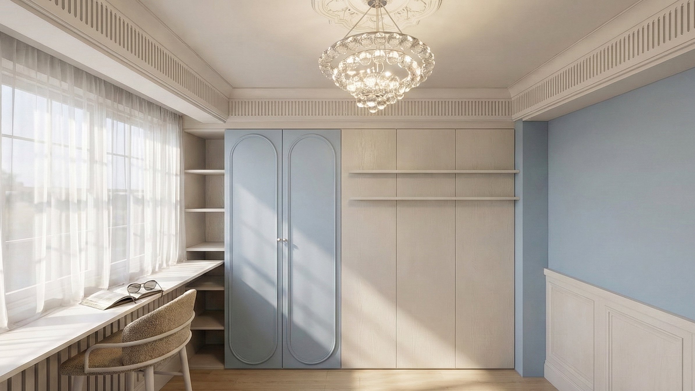 A room with a large window covered by white curtains, a beige desk with open books, and sunglasses on top. Built-in shelves and cabinets in pastel blue and cream are on the wall. A chandelier hangs from the ceiling.