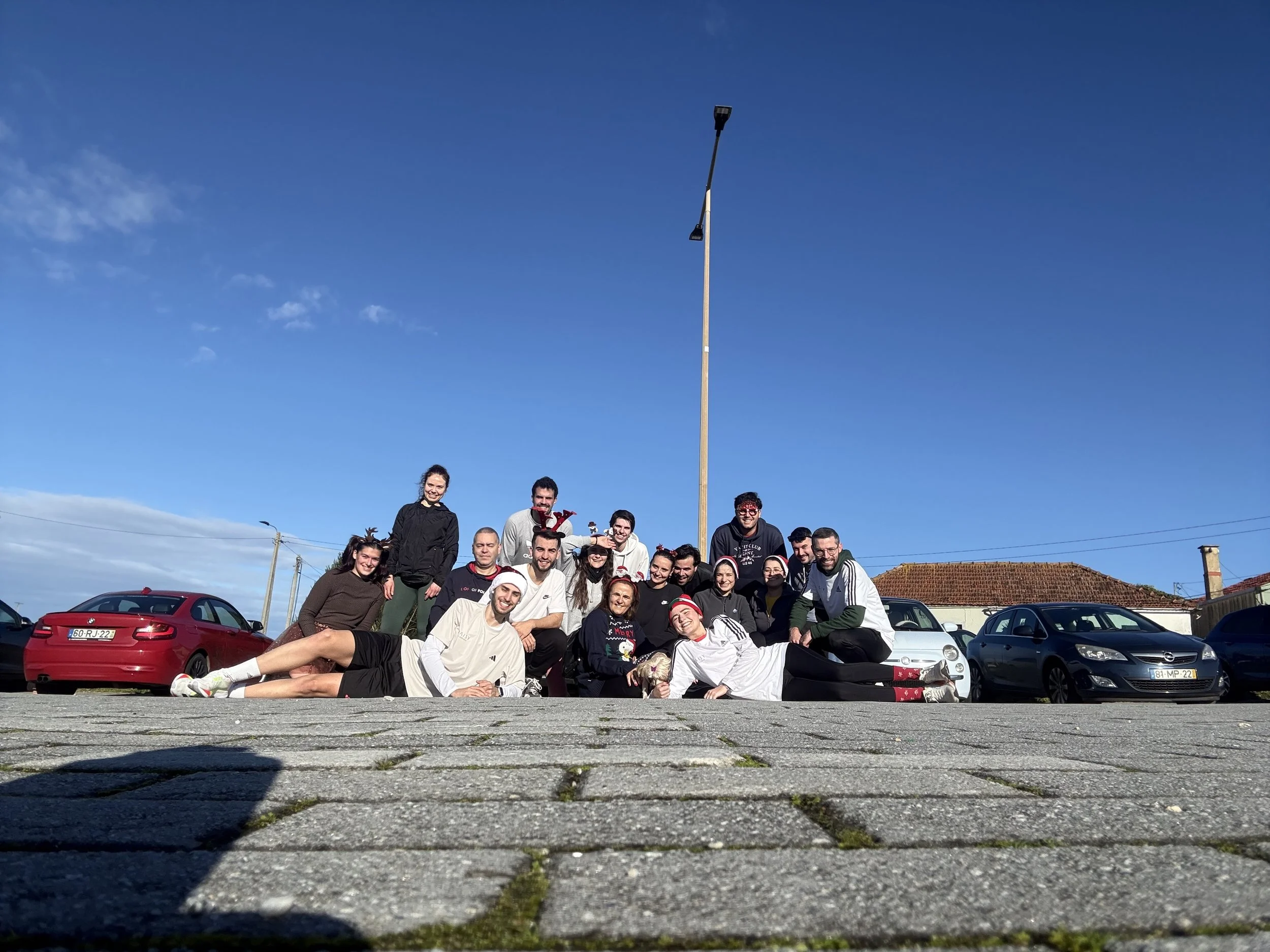 Grupo de pessoas posando ao ar livre em uma rua, com carros atrás, ao pôr do sol ou dia ensolarado.