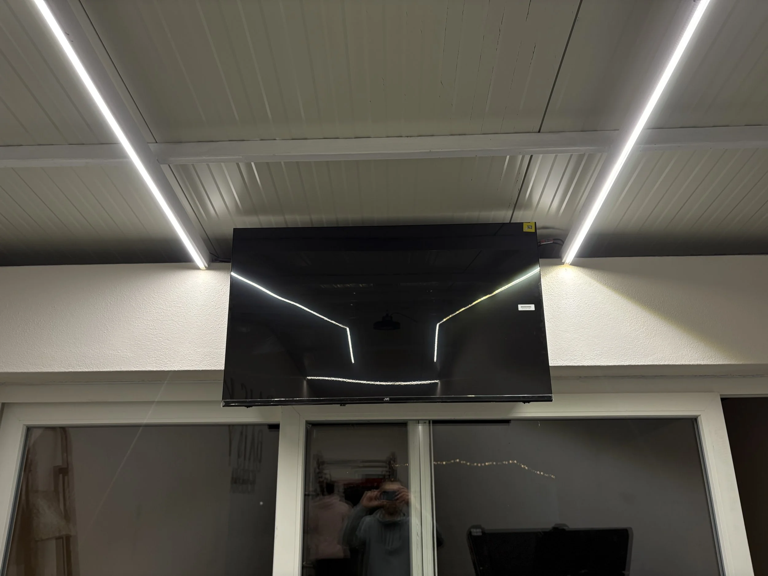 Tela de televisão preta refletindo o teto de uma sala com iluminação de lâmpadas fluorescentes.