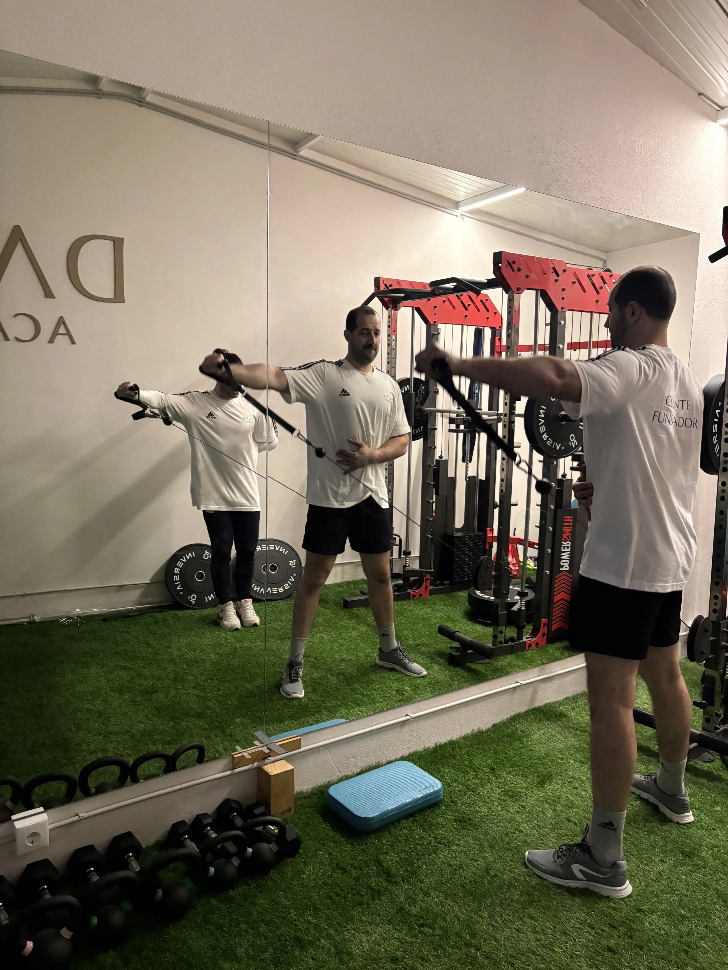 Homem treinando com faixas de resistência em frente a espelho em academia com equipamentos de peso e paredes brancas.