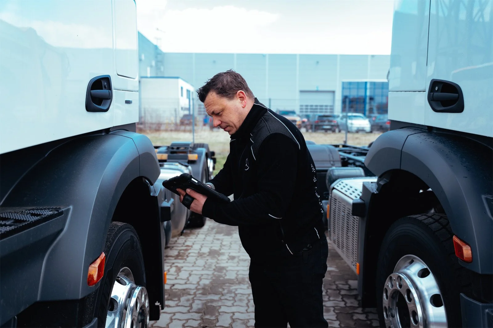 Ein Mann steht zwischen zwei großen Lkw und schaut auf ein mobiles Gerät.