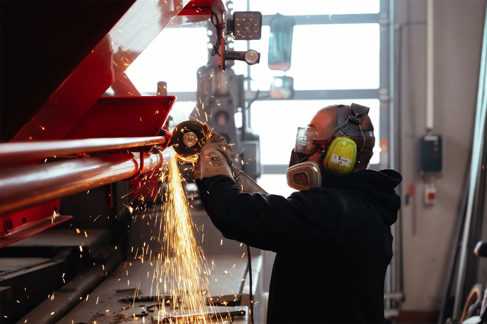 Ein Arbeiter schneidet Metall mit einer Schleifmaschine, Funken fliegen während des Schneidvorgangs, getragen mit Schutzausrüstung.