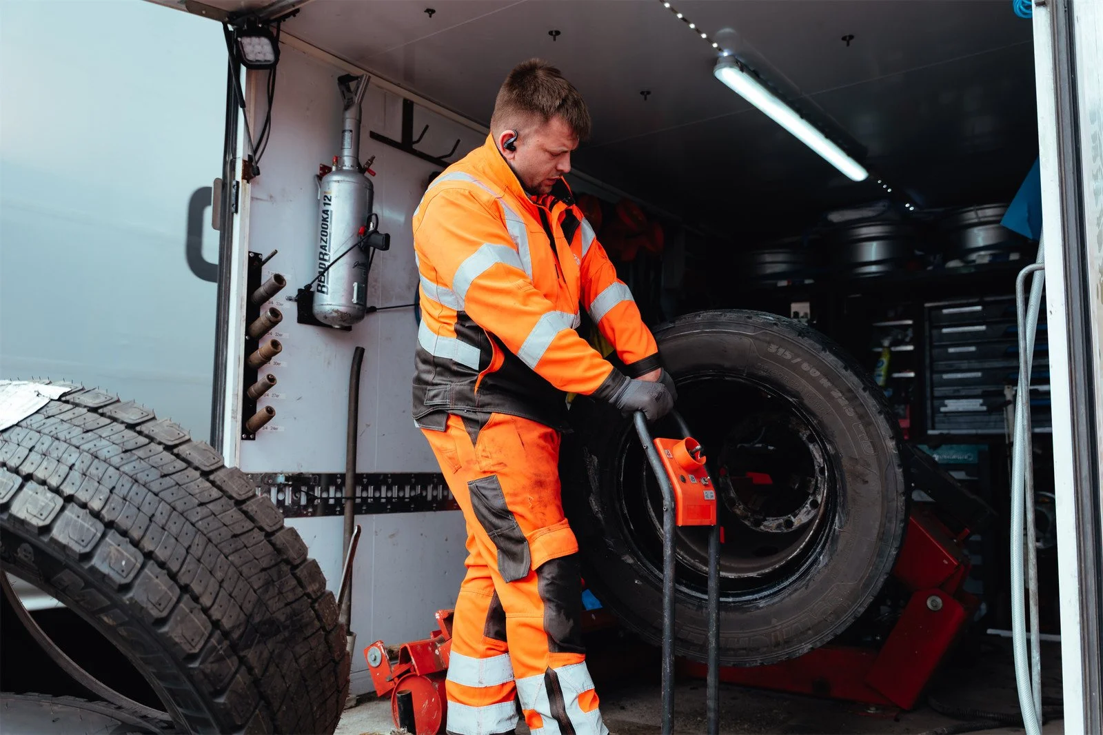 Arbeiter in orange Sicherheitskleidung wechselt einen Reifen in einer Werkstatt oder auf einem Abschleppwagen.