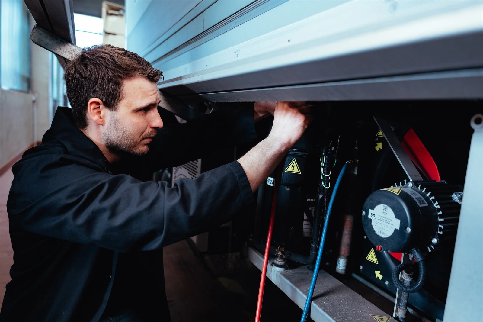 Mann arbeitet an elektrischen Komponenten in einem Technikkasten.