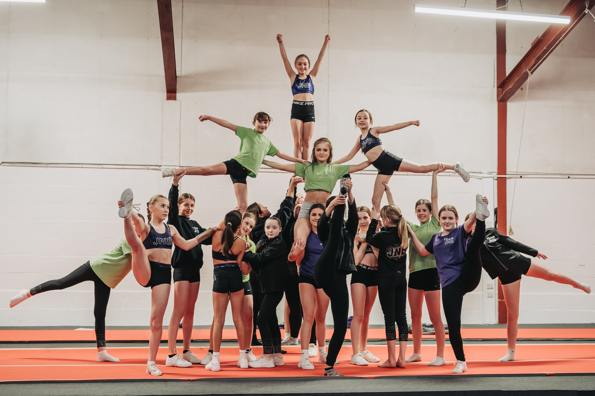 A group of cheerleaders performing a pyramid stunt on a gym mat.