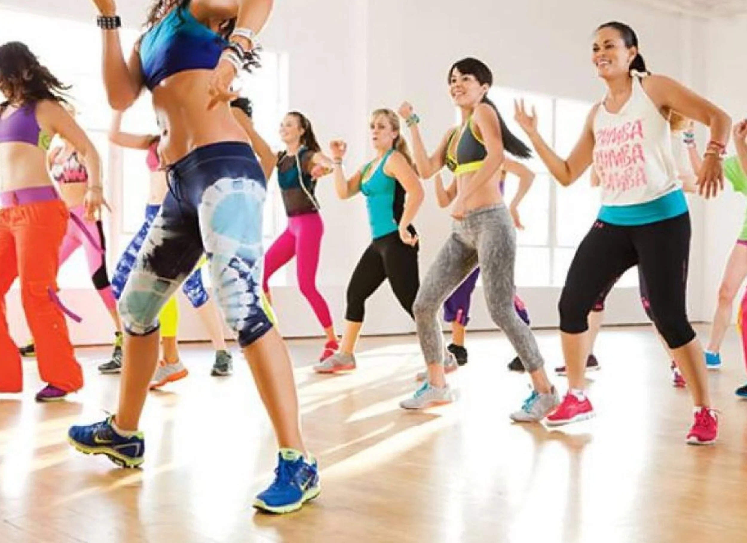 Group of people participating in a vibrant fitness dance class, wearing colorful activewear, in a bright studio.