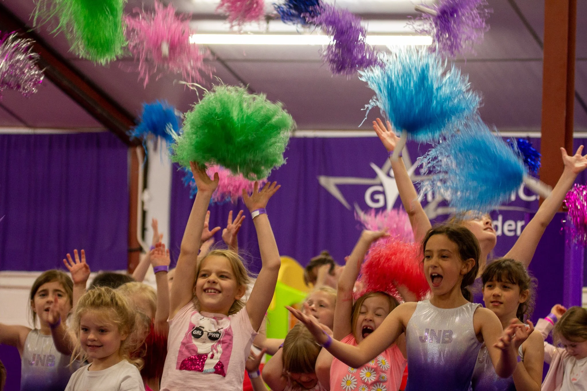 Children celebrating with colorful pom-poms at a gymnastics event.