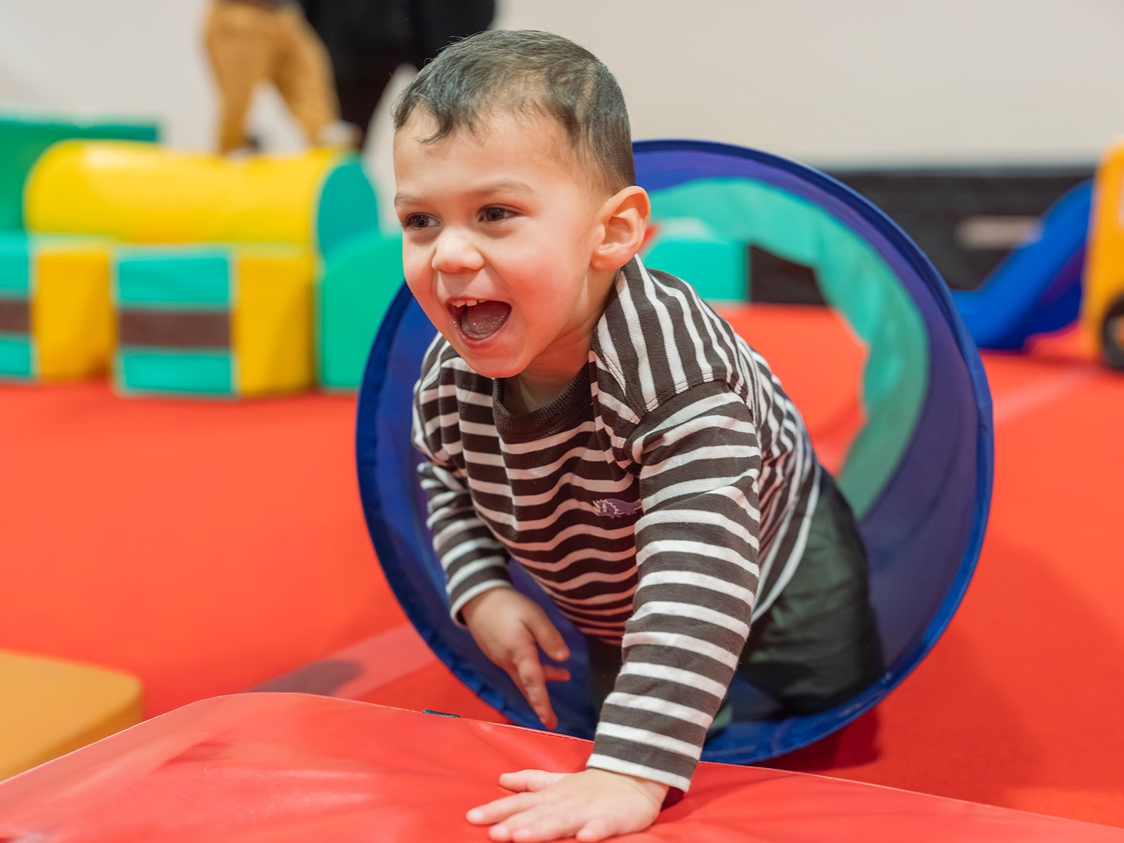 Instructor assisting a young child on a gymnastics wedge mat in a gym setting.