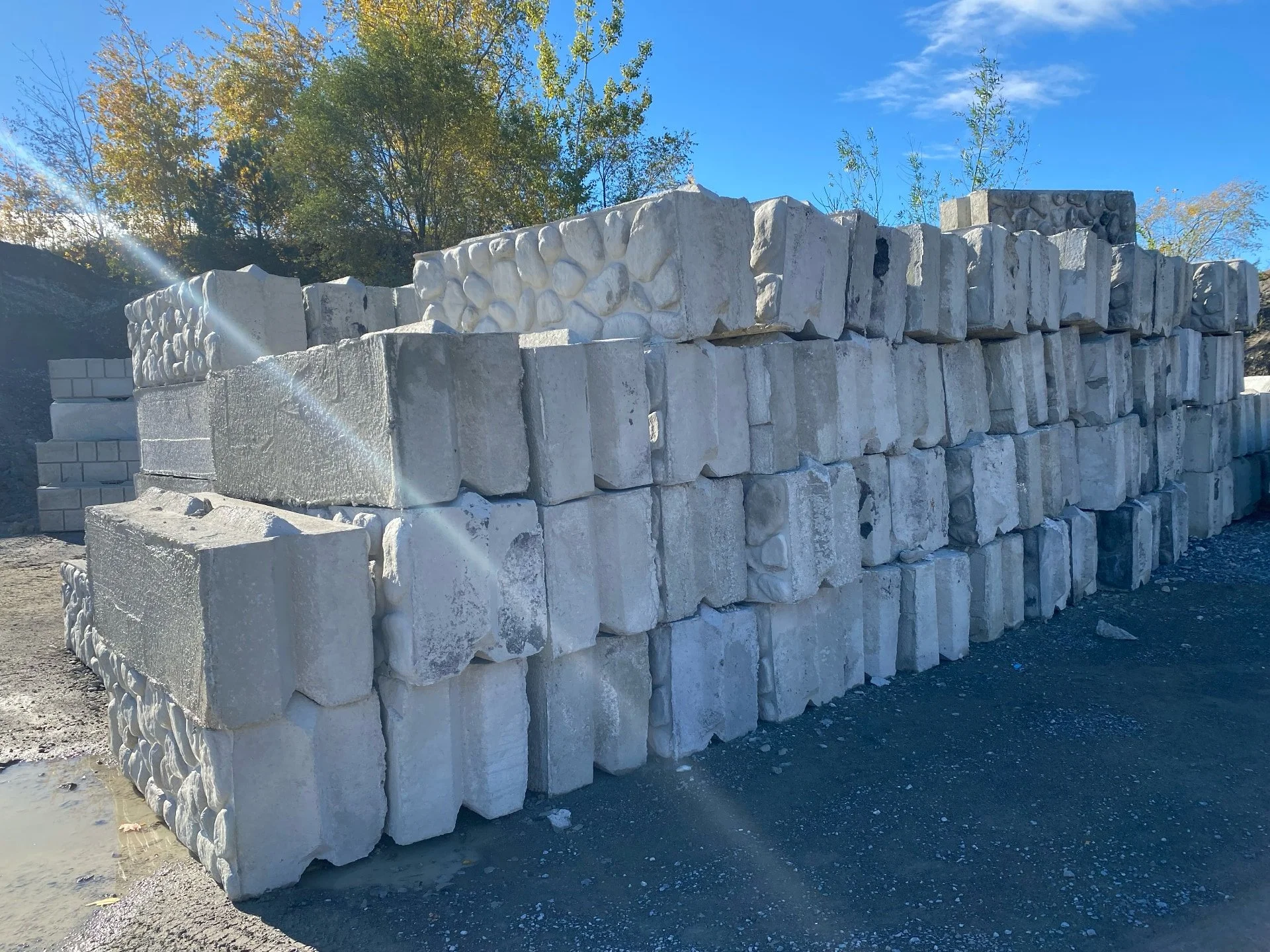 Stacked white stone blocks at a construction site, with trees and blue sky in the background.