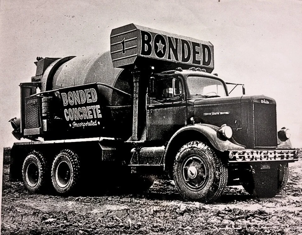 Vintage cement truck with the words "Bonded Concrete" on the side and a large sign reading "Bonded" on top of the truck.
