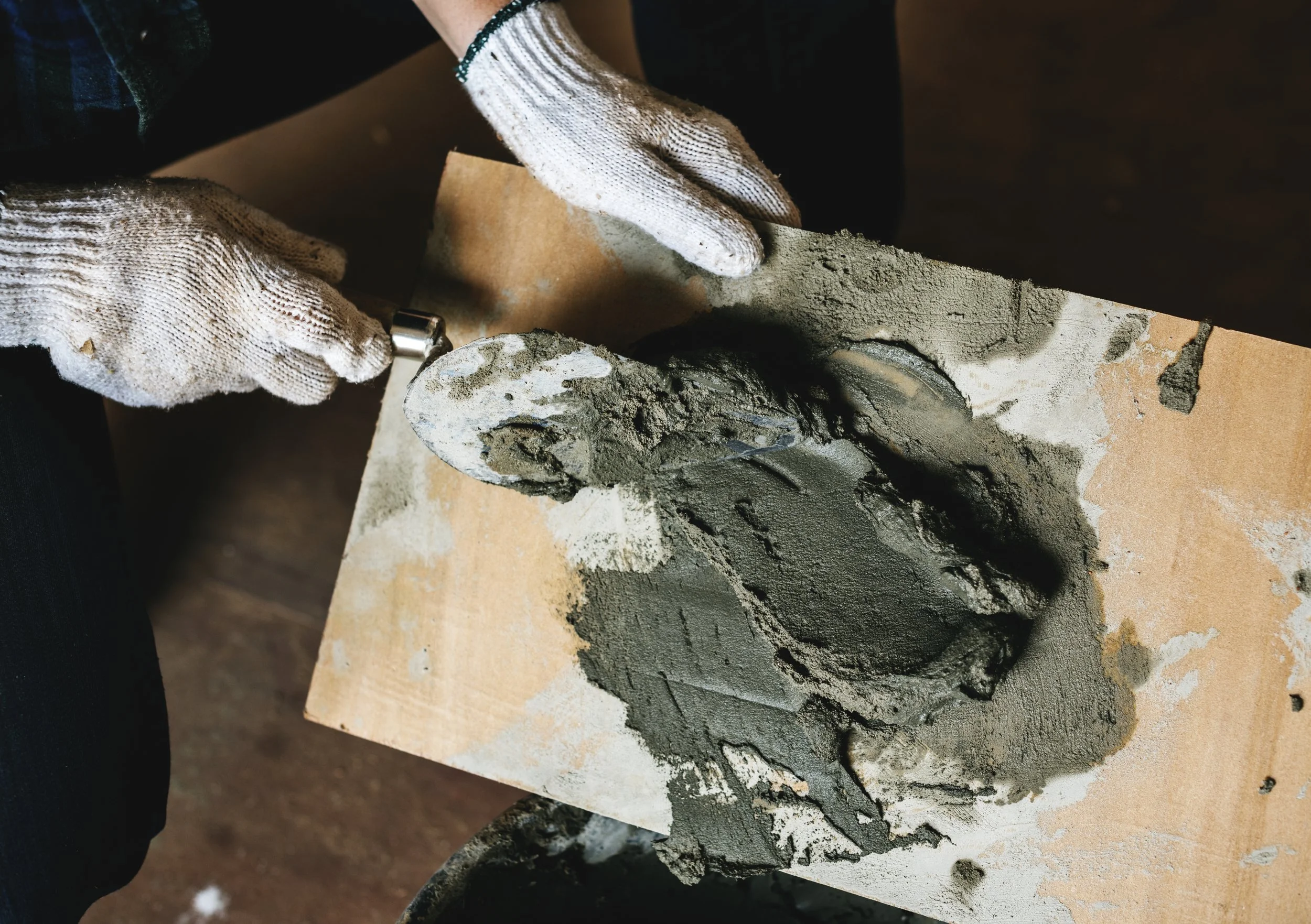 Person wearing gloves chiseling a small stone sculpture on a wooden work surface.