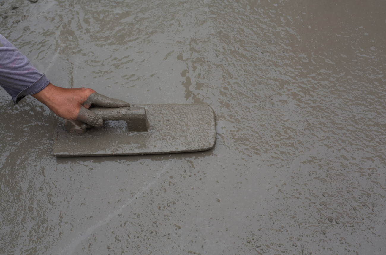 A person wearing a glove is spreading wet cement with a trowel.