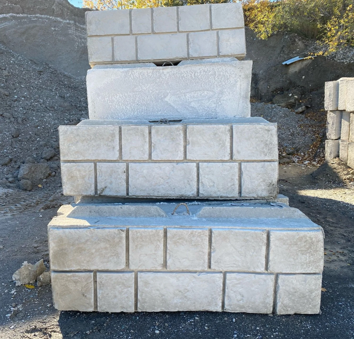 Stacked concrete bricks or blocks on a construction site with dirt and gravel in background.
